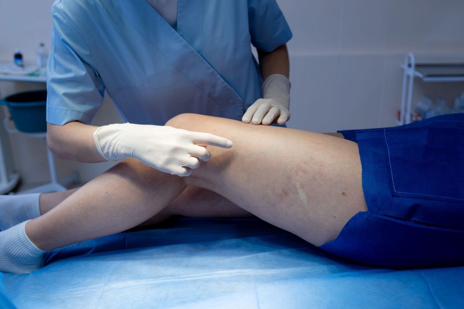 Vein specialist in scrubs and gloves examining a patient's leg during an in-office vein evaluation